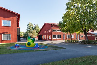 Två träbyggnader i två våningar. På en gräsplan framför syns ett färgglatt konstverk i roliga former. 