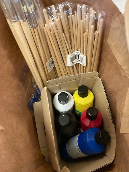 Flaskor med färg och penslar i en pappkasse.
